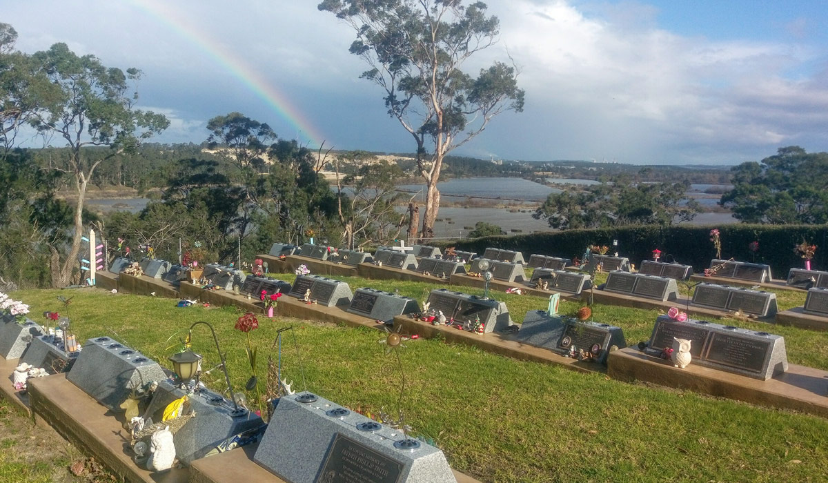 Lawn graves on hillside with rainbow in the sky
