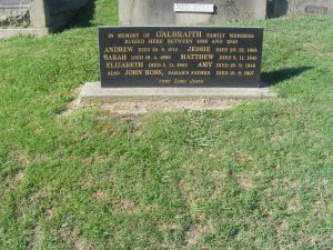 Large black headstone sitting on concrete base on lawn covered grave.