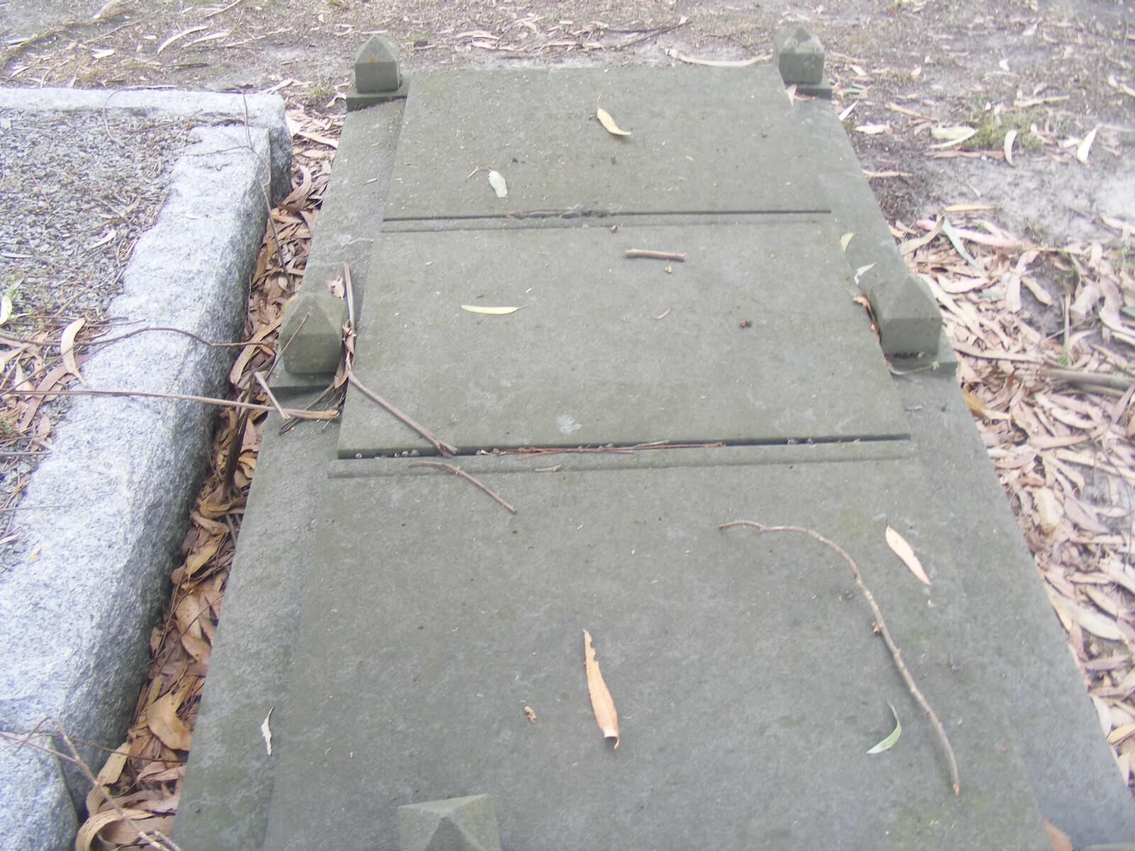 Concrete headstone lying flat on the grand next to another grave edge.